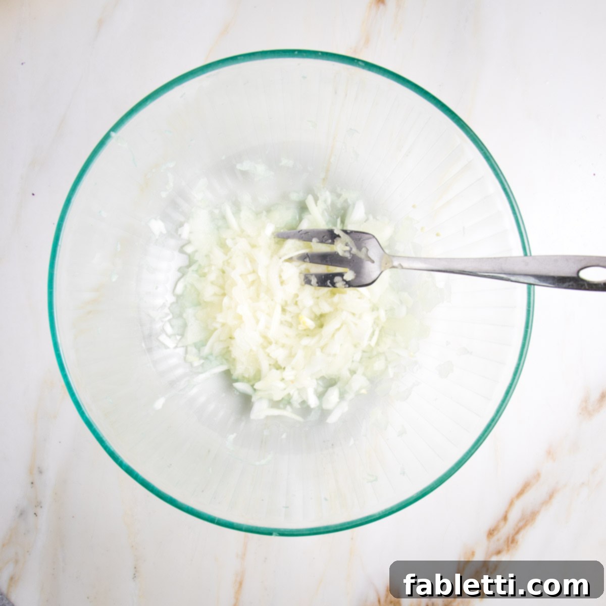 Shredded white onions and juices in a glass bowl.