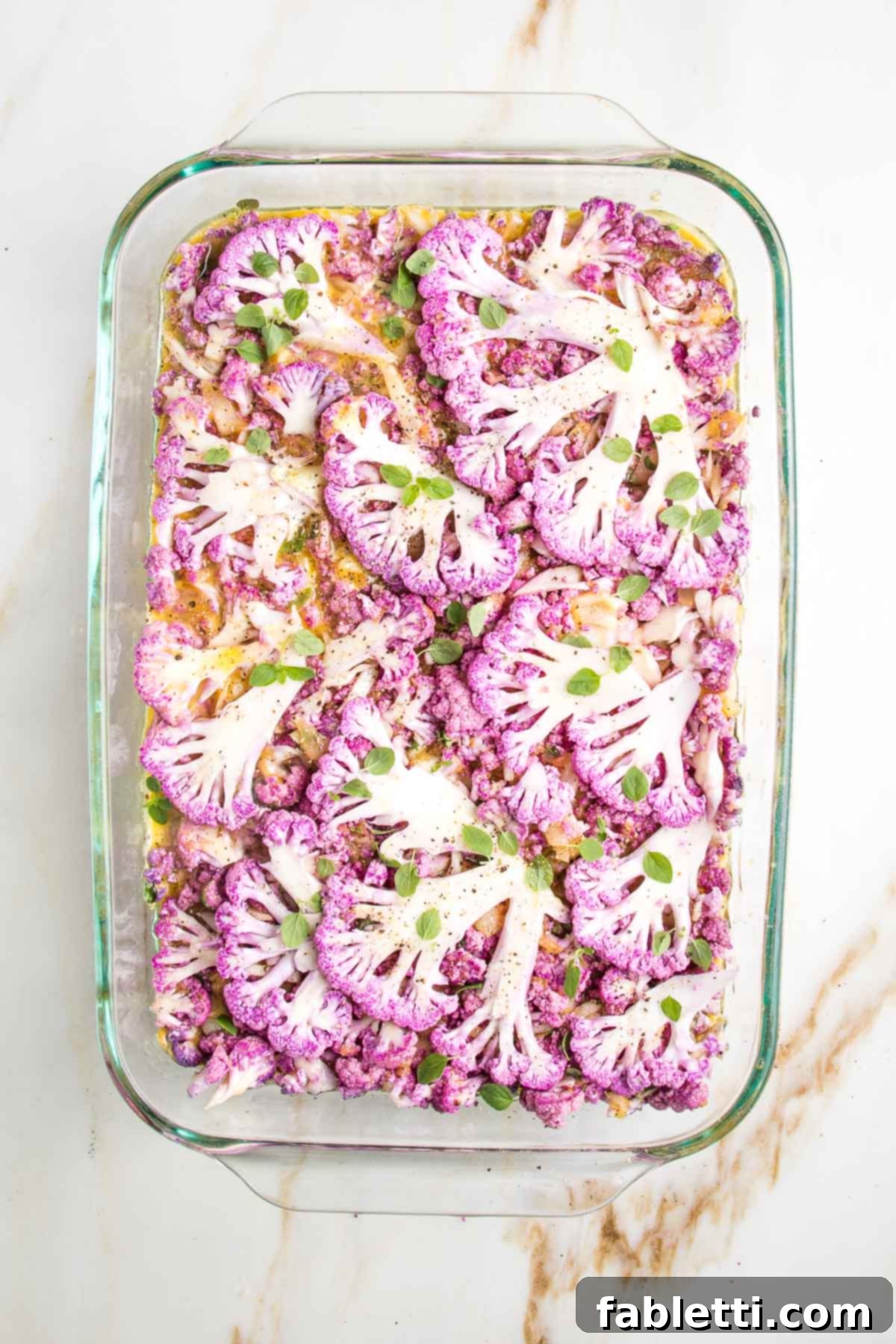Purple cauliflower thinly sliced and placed on the top of a casserole dish filled with cauliflower kugel, ready to bake.
