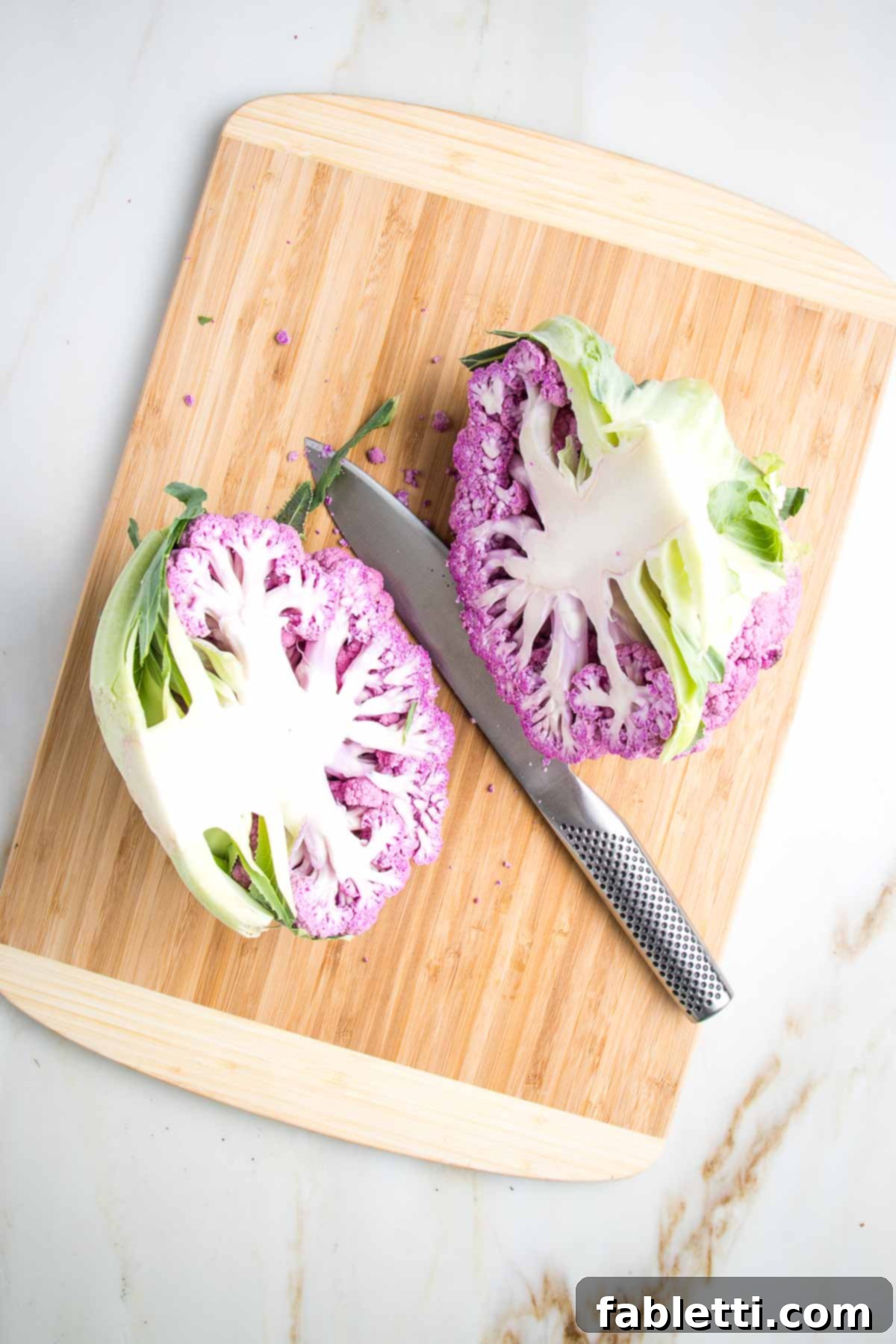 Purple cauliflower cut in half on a wooden board.