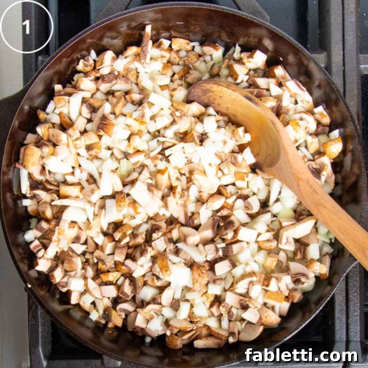 Sun-Kissed Vegan Shepherd's Pie 11 Diced onions and mushrooms in a cast iron skillet with a wooden spoon.