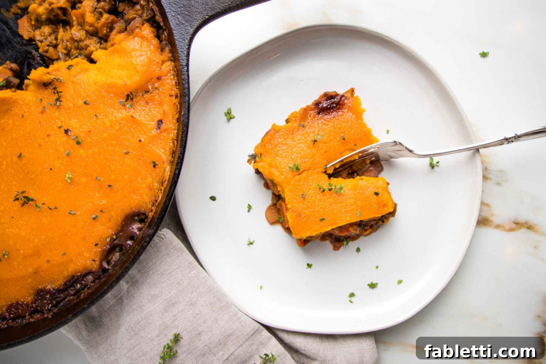 Sun-Kissed Vegan Shepherd's Pie 20 Skillet shepherd's pie on left with a white plate holding a piece of shepherd's pie topped with sweet potato mash, sprinkled with fresh thyme.