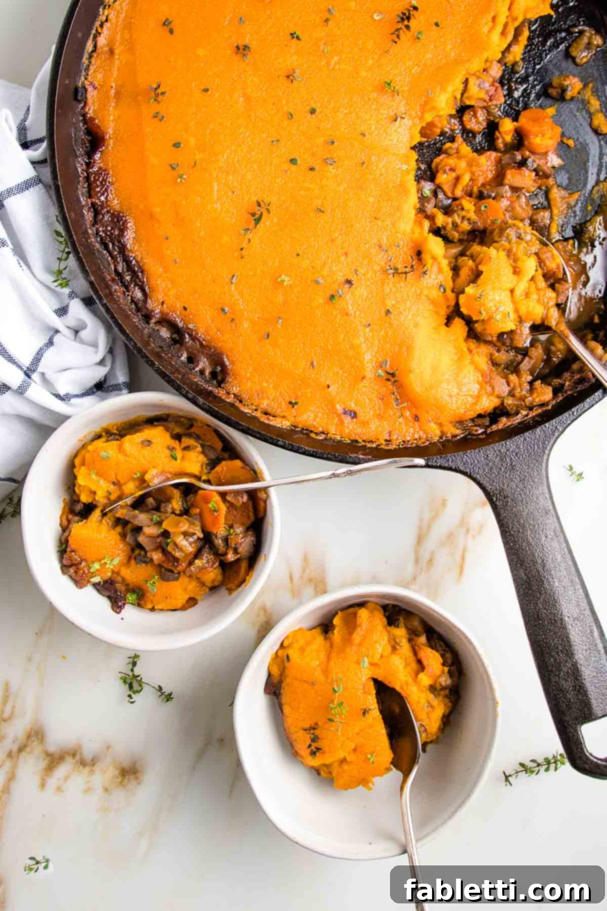 Sun-Kissed Vegan Shepherd's Pie 3 Cast iron skillet filled with lentil shepherds pie topped with sweet potato mash. Two small bowls with servings of vegan shepherd's pie on the bottom left of photo.
