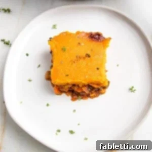 Sun-Kissed Vegan Shepherd's Pie 21 White rimmed plate with a square of veggie shepherd's pie, topped with sweet potato mash, sprinkled with fresh thyme.