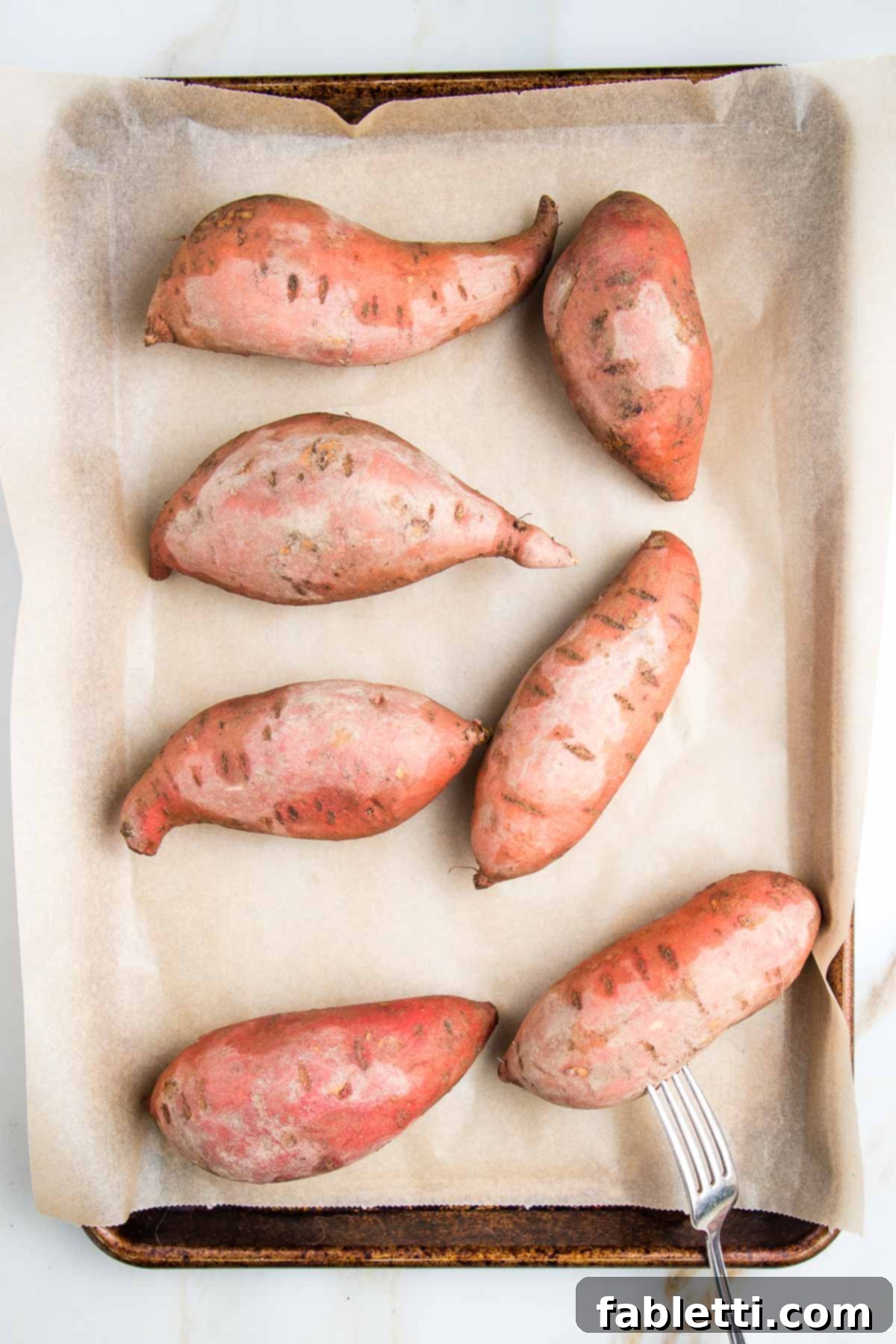 Sun-Kissed Vegan Shepherd's Pie 5 Whole sweet potatoes pricked with a fork on a parchment lined baking sheet.