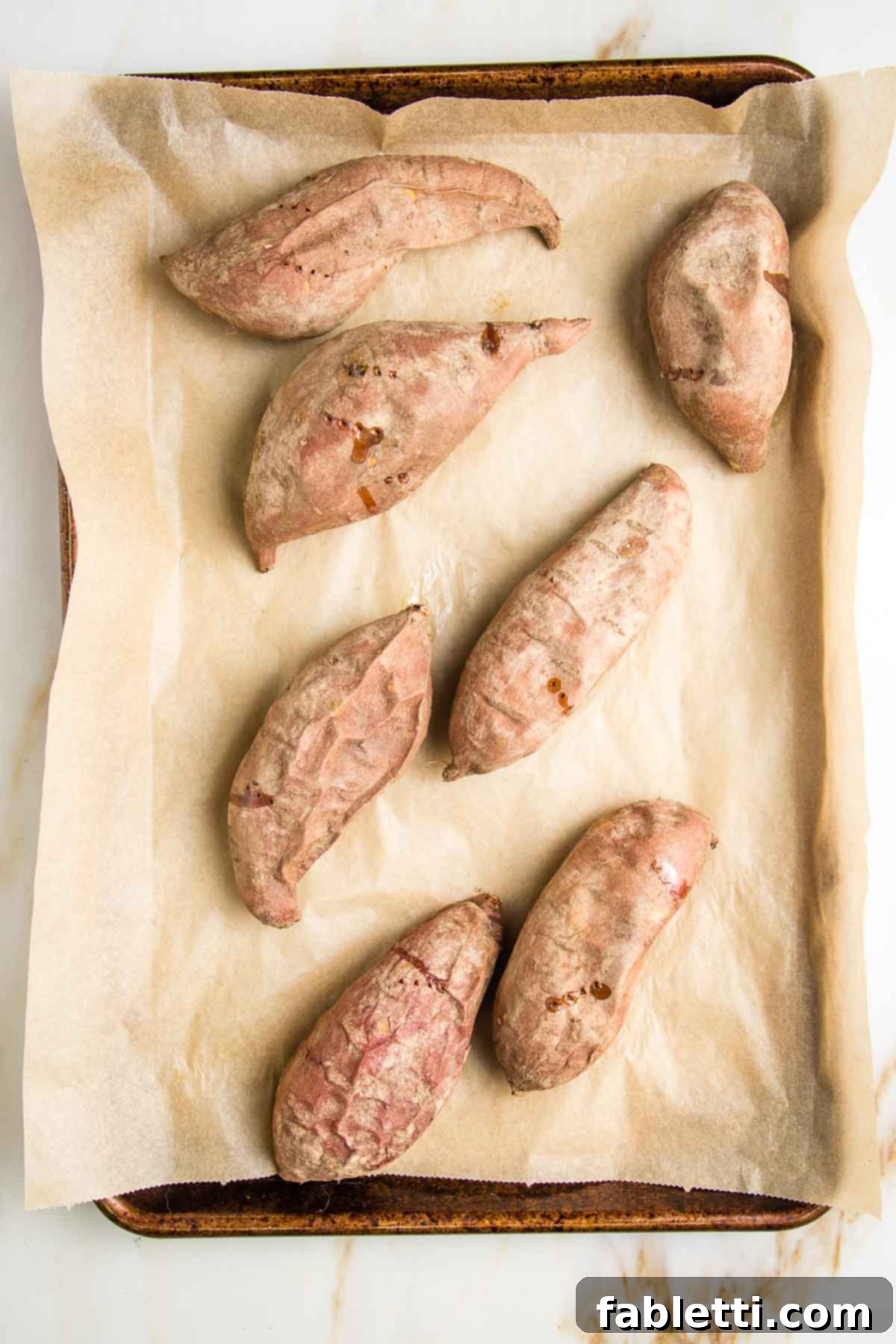 Sun-Kissed Vegan Shepherd's Pie 6 Shriveled baked sweet potatoes on a parchment lined baking sheet.