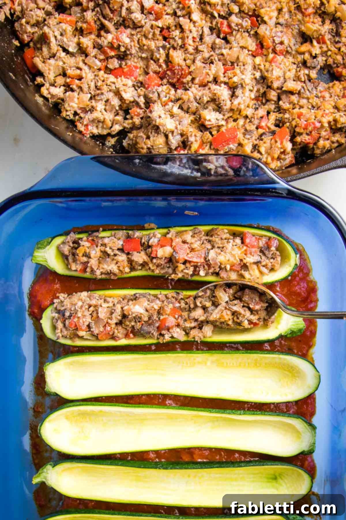 Satisfying Plant-Powered Zucchini Boats 12 A close-up view of the pan's edge reveals the rich, vegan 'meaty' filling, ready to be scooped. In the background, a baking dish holds the par-baked zucchini boats, which are currently being generously filled with the savory mixture.