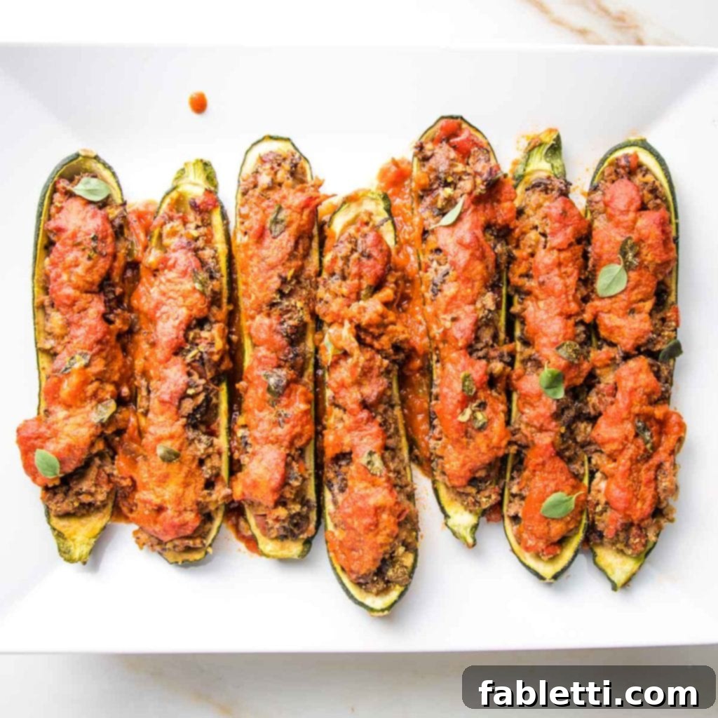 Satisfying Plant-Powered Zucchini Boats 16 An appetizing close-up of zucchini boats, generously stuffed with a savory plant-based filling, beautifully topped with marinara sauce and fresh herbs, ready to be enjoyed.
