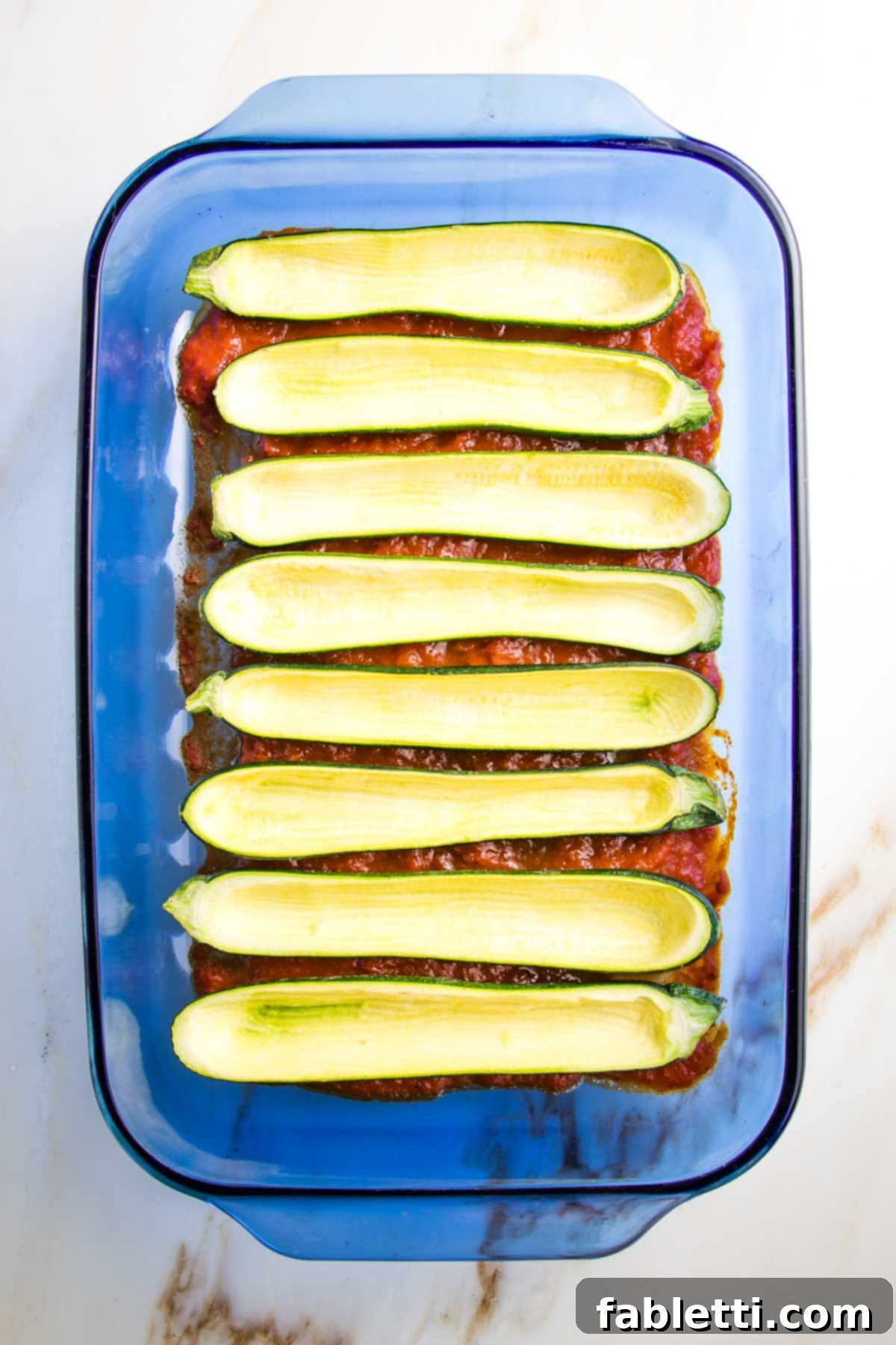 Satisfying Plant-Powered Zucchini Boats 5 A 9x13 inch baking dish coated with a thin layer of marinara sauce, precisely arranged with several empty, hollowed-out zucchini boats, ready for their pre-bake in the oven.