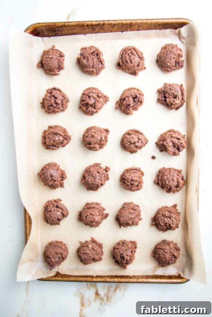 Irresistible Cookie Dough Poppers 12 chocolate cookie dough balls scooped onto a rimmed baking tray lined with parchment paper