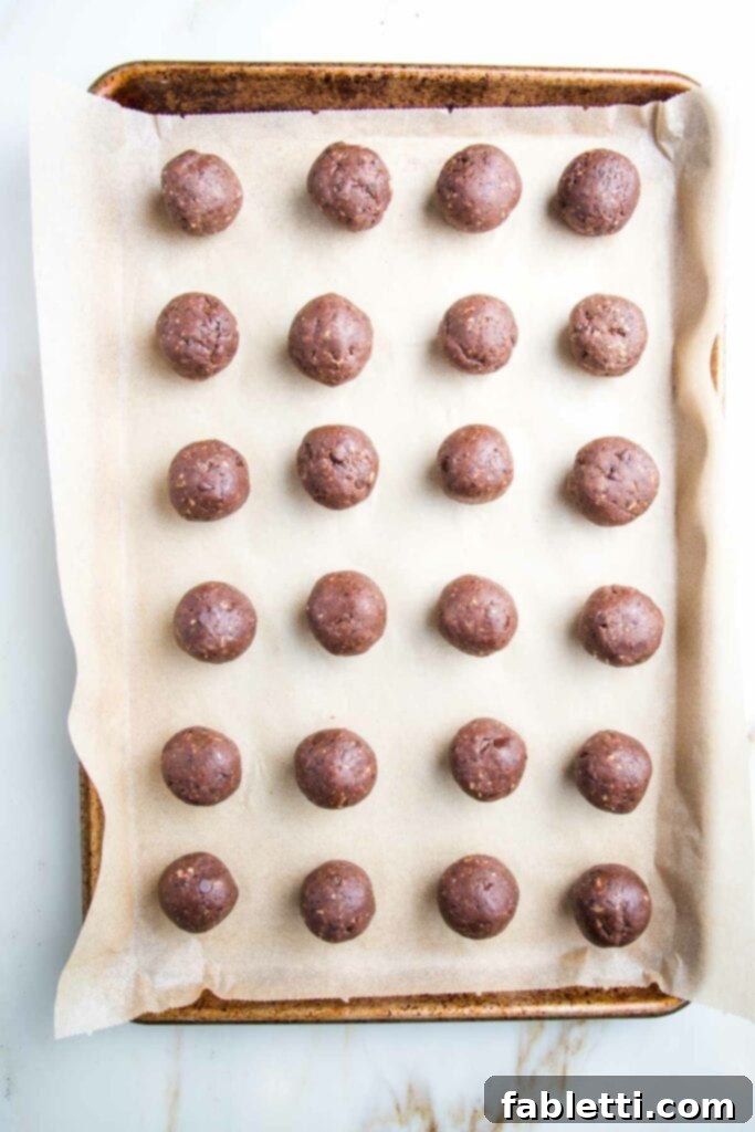 Irresistible Cookie Dough Poppers 13 Rimmed baking tray, lined with parchment, neat rows of chocolate cookie balls lined up on tray.