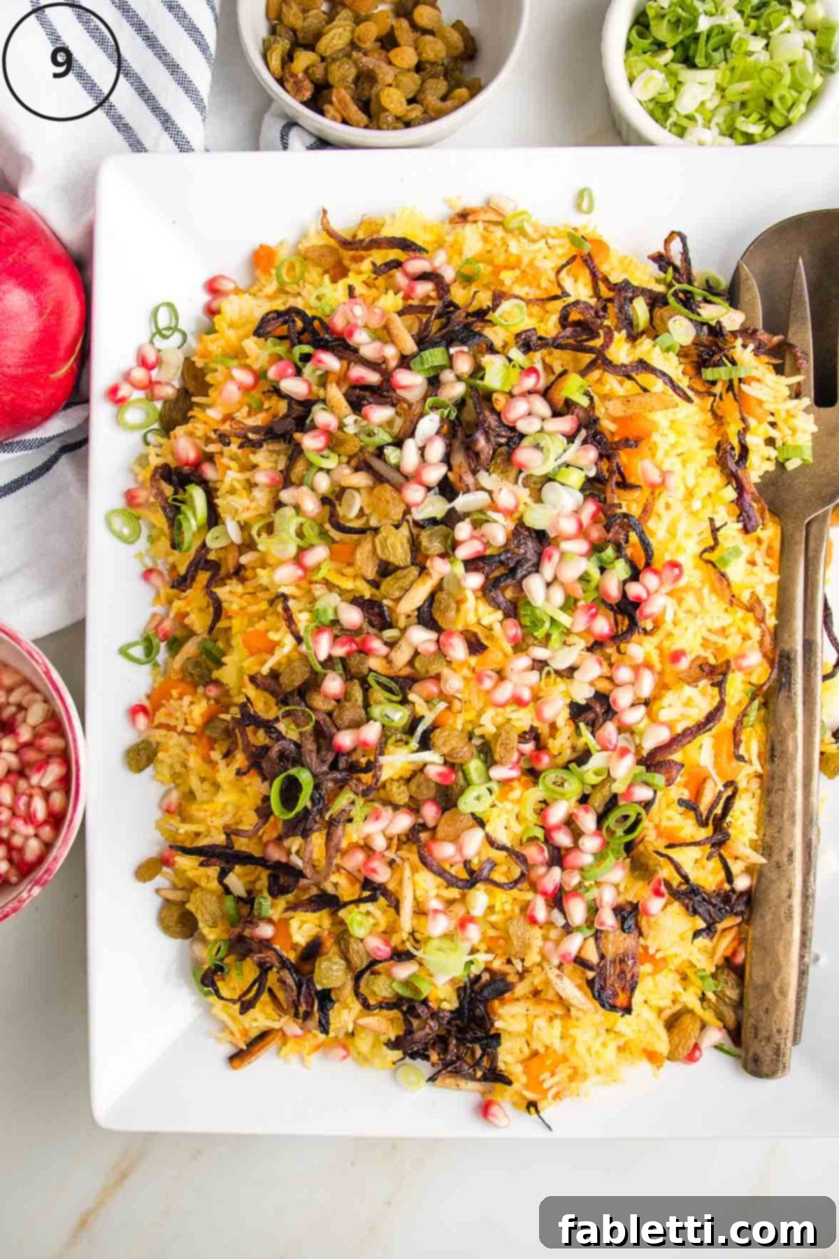 Jeweled Rice layered onto a platter with caramelized onions, scallions, pomegranate seeds, raisins and nuts.