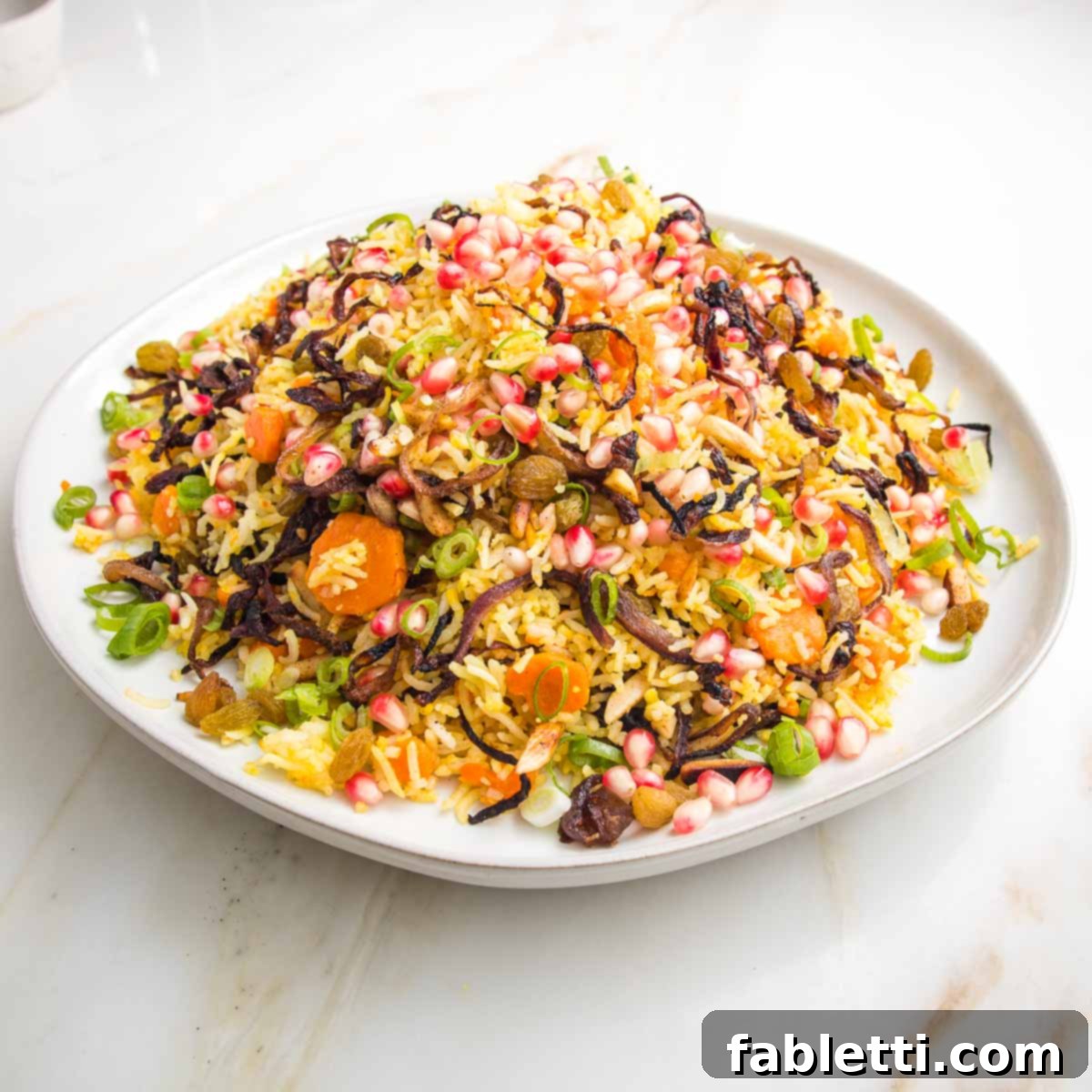 White rimmed plate filled with jeweled rice: rice, carrots, raisins, caramelized onions, almonds, scallions.