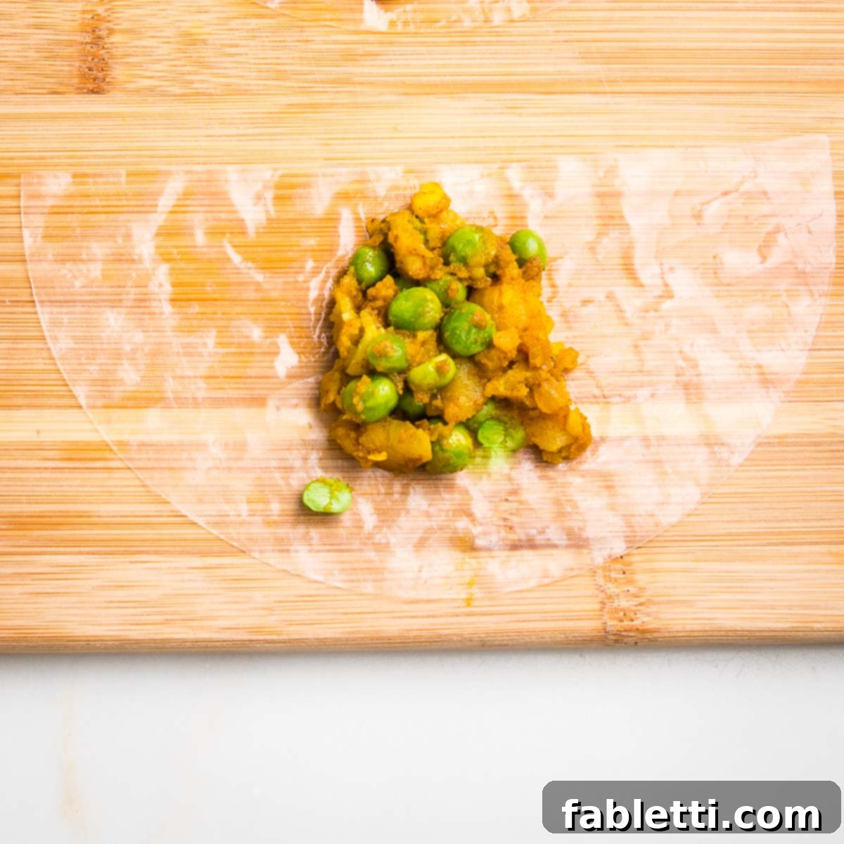 Crispy Baked Samosas with Zesty Cilantro Chutney 11 Half moon of moistened rice paper on a wooden board with a scoop of potato samosa filling