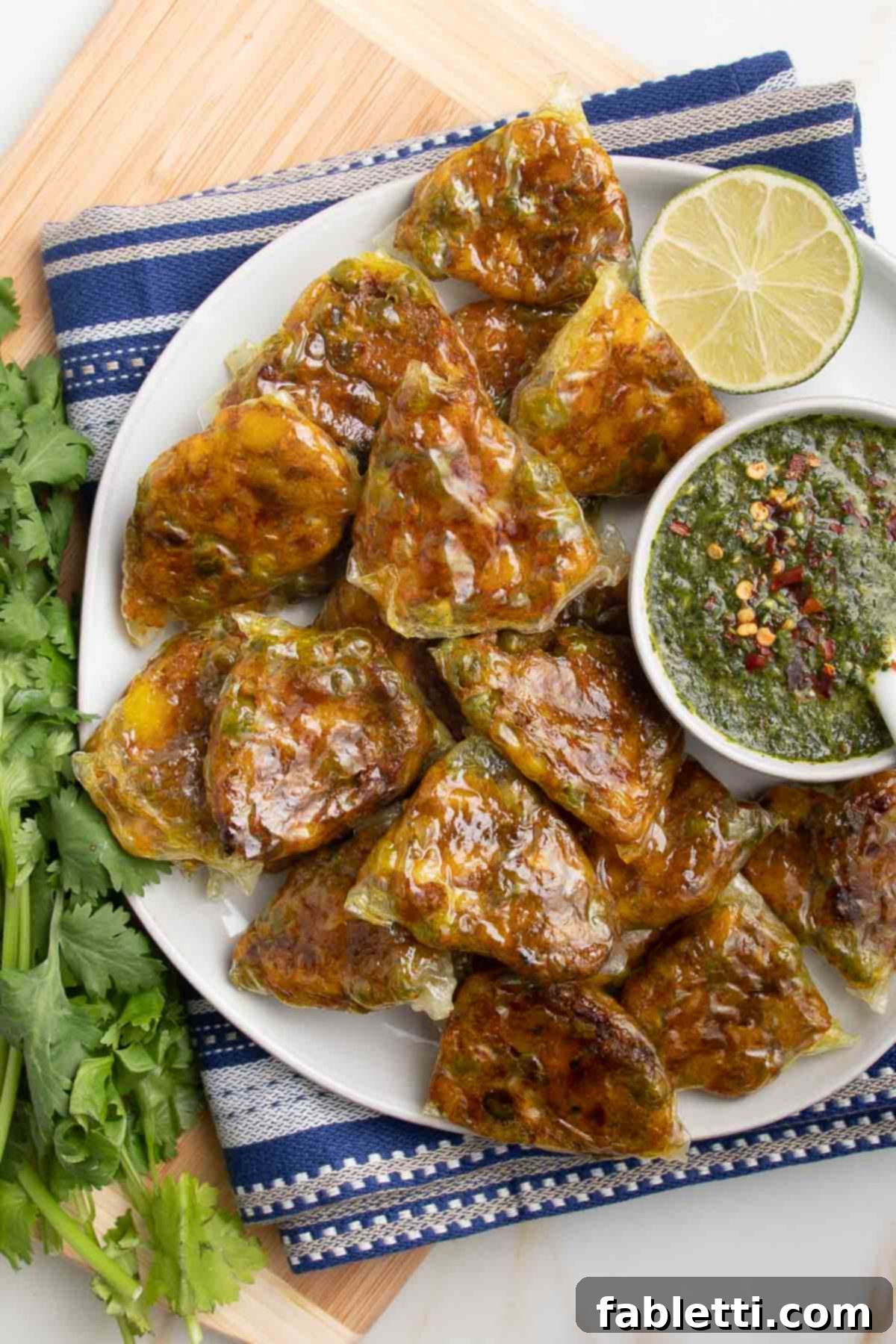 Crispy Baked Samosas with Zesty Cilantro Chutney 18 White plate, filled with mini baked samosas with a small dish of green chutney dipping sauce.