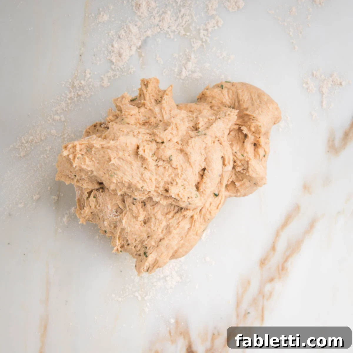Fluffy Vegan Dinner Rolls 12 Rough, shaggy looking, blob of dough on a marble counter dusted with flour.