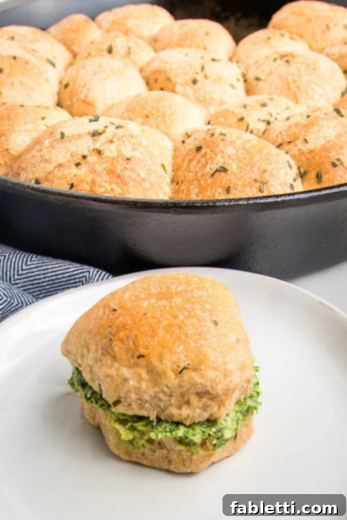 Fluffy Vegan Dinner Rolls 4 Close up of a sandwich roll stuffed with pesto and in the background a cast iron pan filled with more herby rolls.