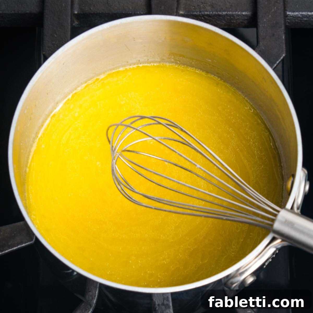 Fluffy Vegan Dinner Rolls 5 Small saucepan with a yellow liquid being stirred with a wire whisk.