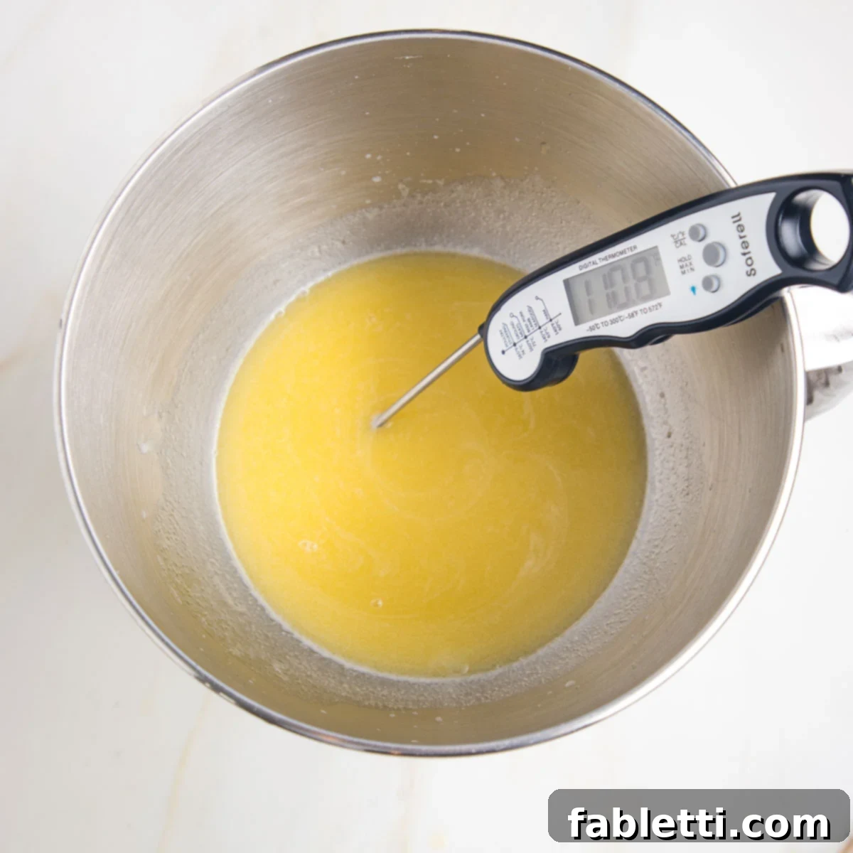 Fluffy Vegan Dinner Rolls 6 Stainless steel bowl of stand mixer with yellow liquid. There is a thermometer reading 110.8 degrees inserted into the liquid.