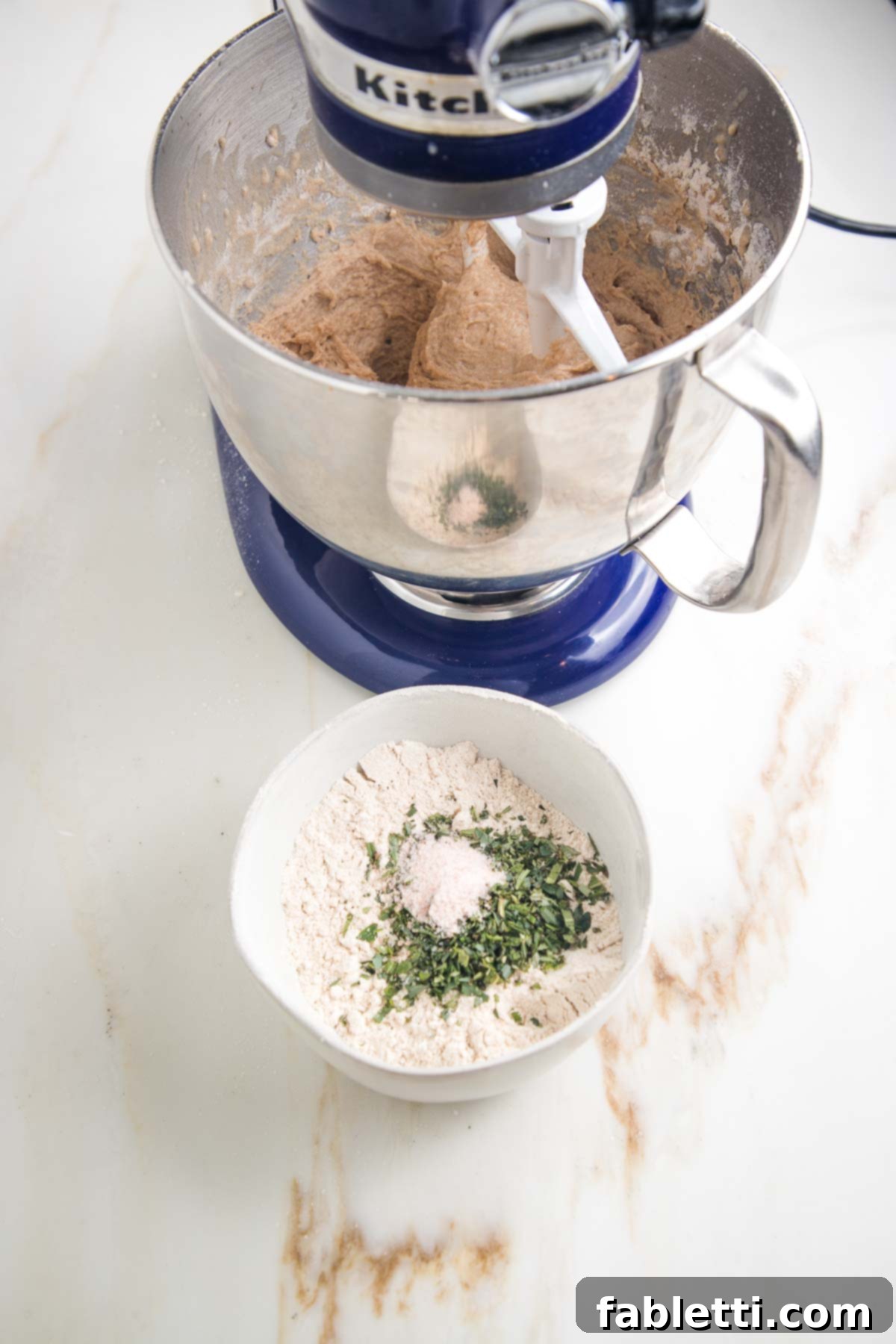 Fluffy Vegan Dinner Rolls 10 Blue stand mixer making dough. Small bowl with flour and chopped fresh herbs in the foreground