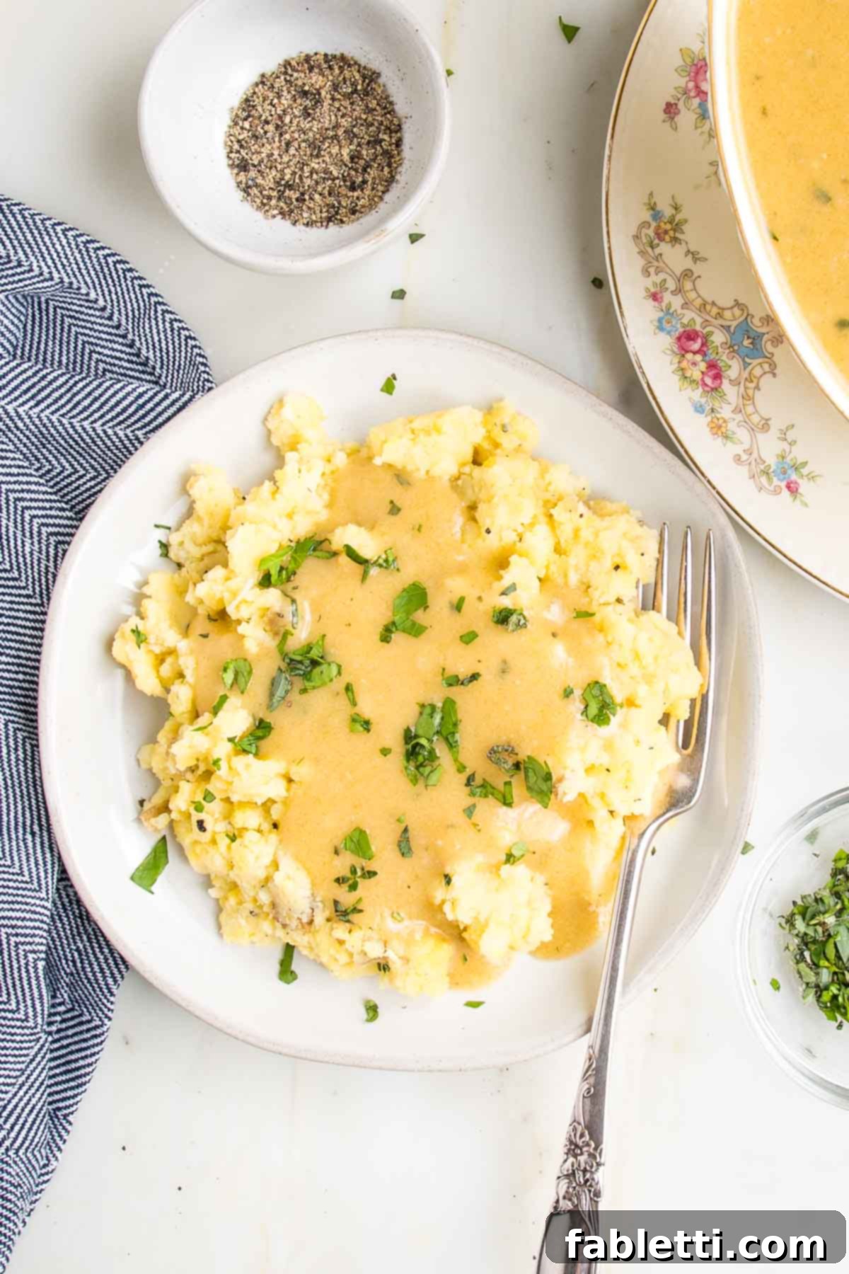 Whip Up Perfect Vegan Gravy 3 A beautifully plated dish of mashed potatoes generously covered in golden vegan gravy and garnished with a sprinkle of fresh vibrant green herbs. The scene is appetizing and highlights the rich texture of the gravy.