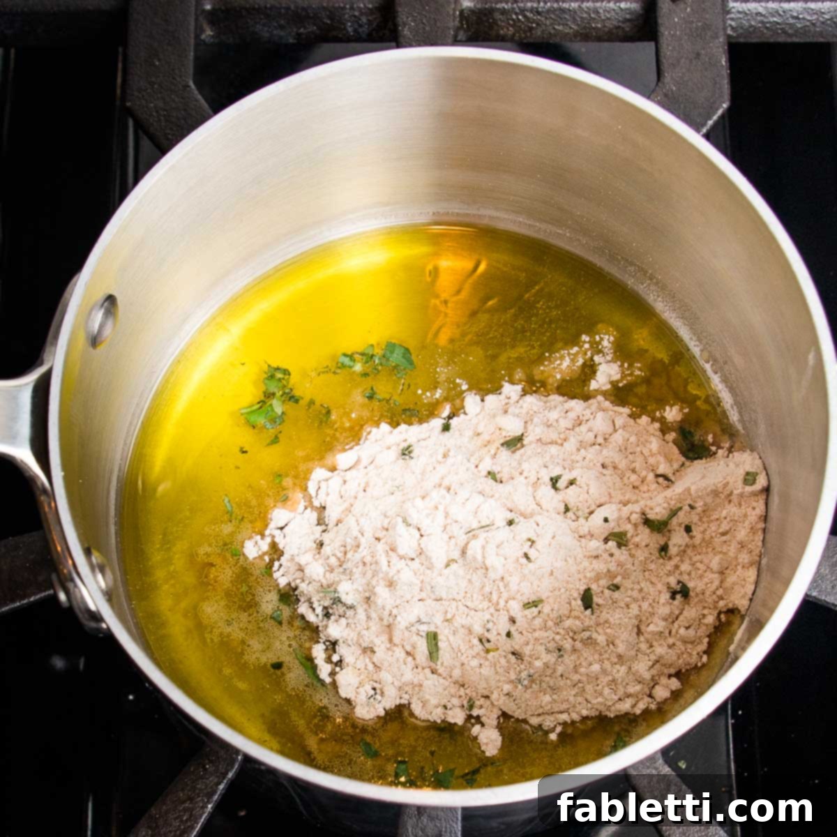 Whip Up Perfect Vegan Gravy 6 A small saucepan on a stove with olive oil heating, preparing for the roux. A small pile of the dry flour and herb mixture is visible on one side, awaiting to be whisked in.