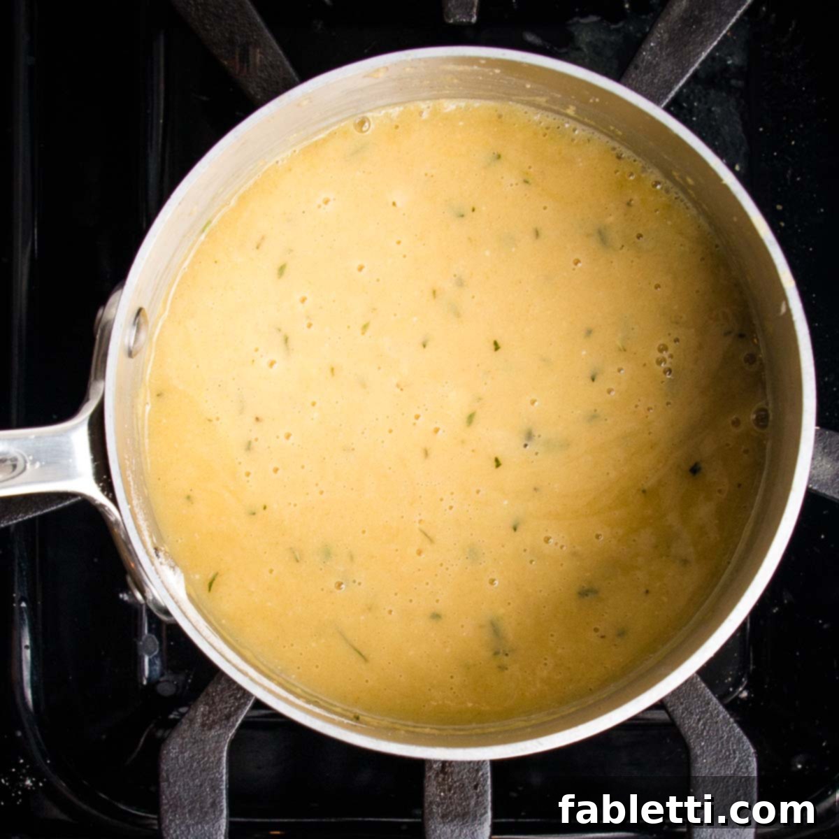Whip Up Perfect Vegan Gravy 9 A small saucepan filled with rich, golden vegan gravy, perfectly thickened and speckled with vibrant fresh herbs, resting on a stove. The gravy appears smooth and ready to serve, highlighting its inviting texture and color.