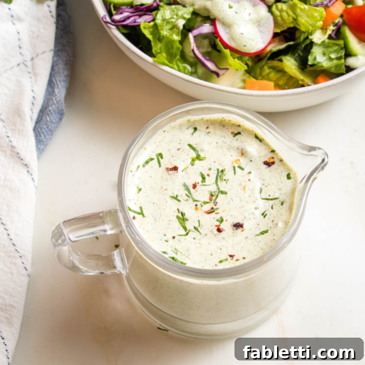 Deliciously Healthy Homemade Ranch 6 A close-up view of a small, elegant glass pitcher brimming with creamy, luscious vegan ranch dressing, ready to be served.