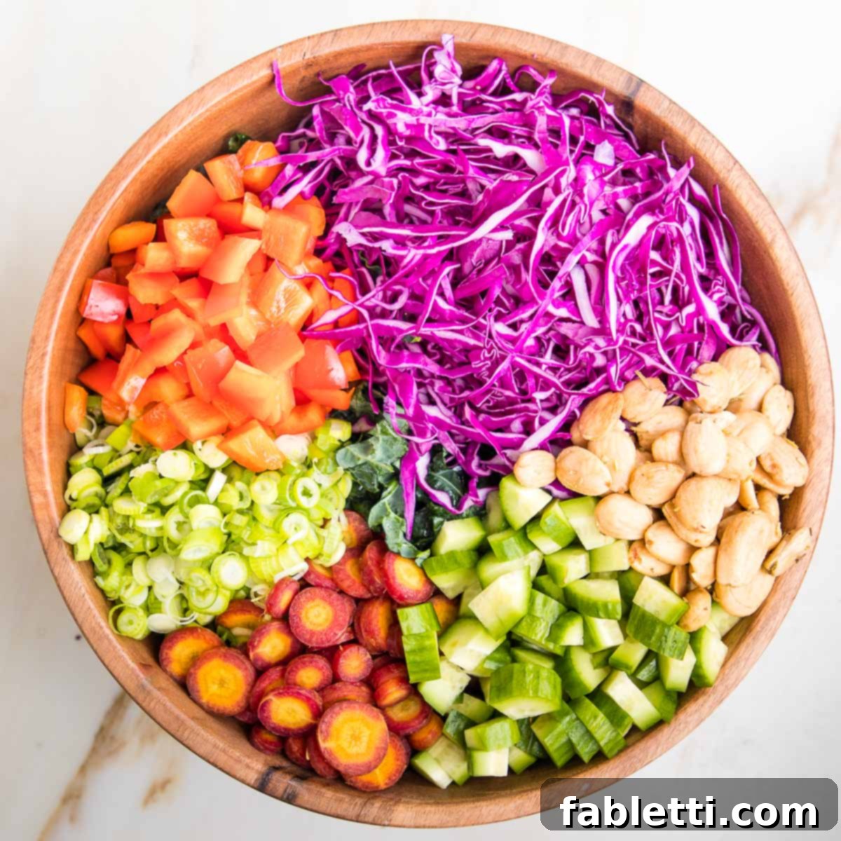 Rustic Tuscan Chopped Kale Medley 10 Wooden salad bowl filled with chopped kale and then sections of chopped veggies are on top of the kale. Purple cabbage, red peppers, scallions, purple carrots, cucumbers and marcona almonds