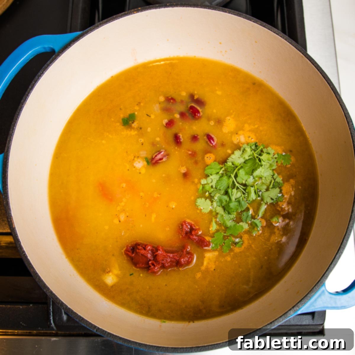 Hearty Vegan Taco Soup with Crispy Tortilla Strips 13 dutch oven filled with broth, tomato paste, beans, fresh cilantro.