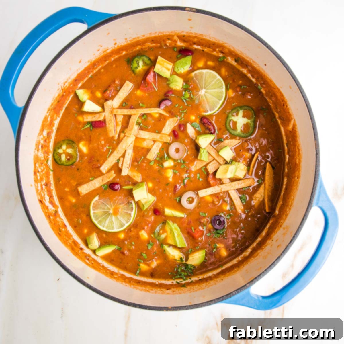 Hearty Vegan Taco Soup with Crispy Tortilla Strips 18 Bright and vibrant vegan tortilla soup. Dutch oven is filled with tomato based soup and decorated with chunks of avocado, lime wedges, sliced jalapenos and olives, plus baked tortilla strips.