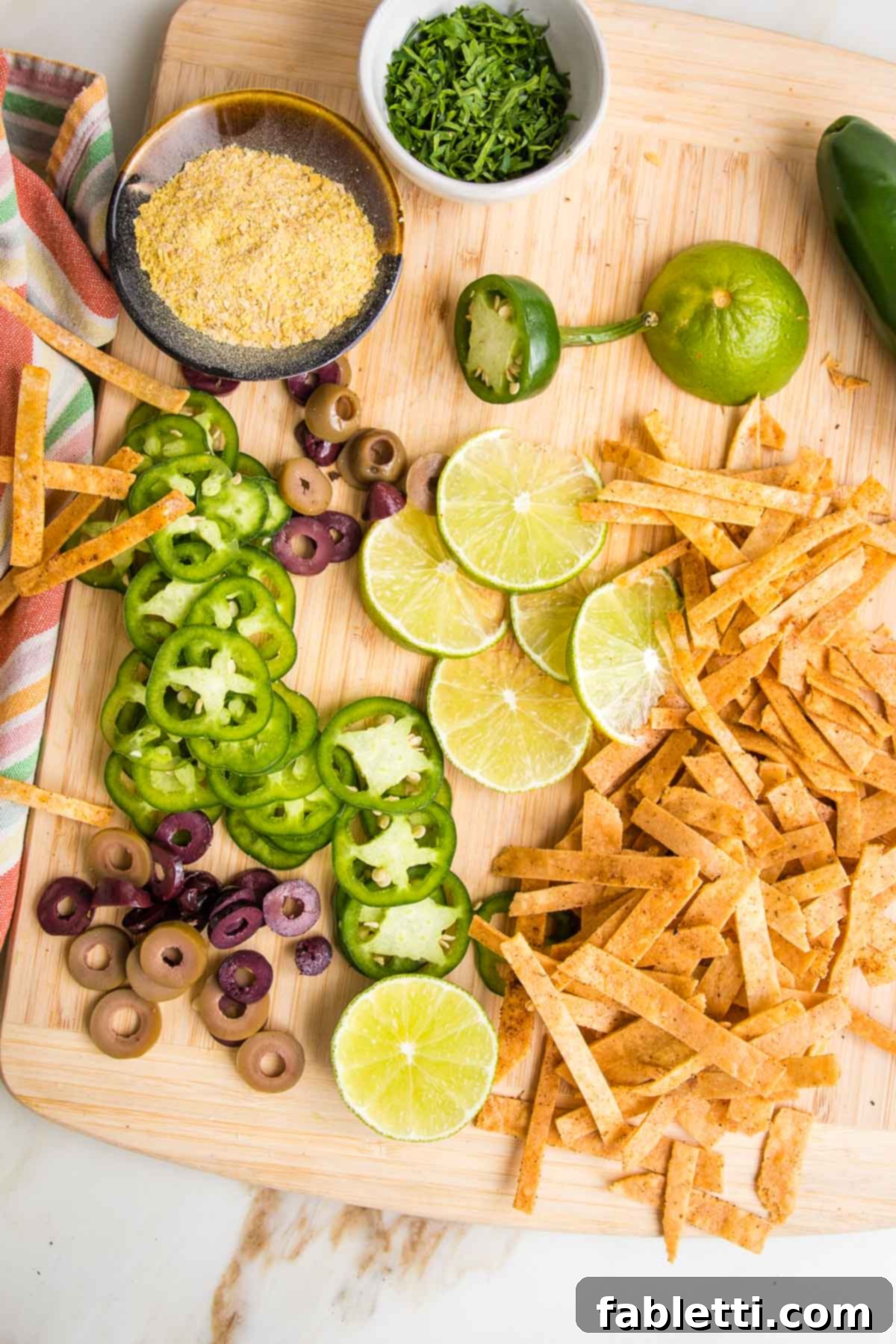 Hearty Vegan Taco Soup with Crispy Tortilla Strips 19 Cutting board with garnishes for vegan taco soup: sliced jalapenos, nutritional yeast, lime wedges, chopped fresh jalapenos, baked tortilla strips.