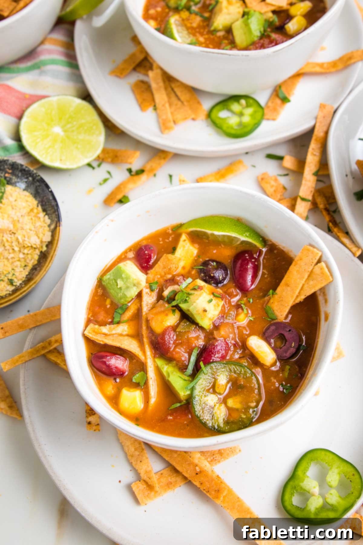 Hearty Vegan Taco Soup with Crispy Tortilla Strips 4 Close up of a bowl of taco soup with bright veggies on top...avocado chunks, corn, sliced olives and jalapenos, plus baked tortilla strips.
