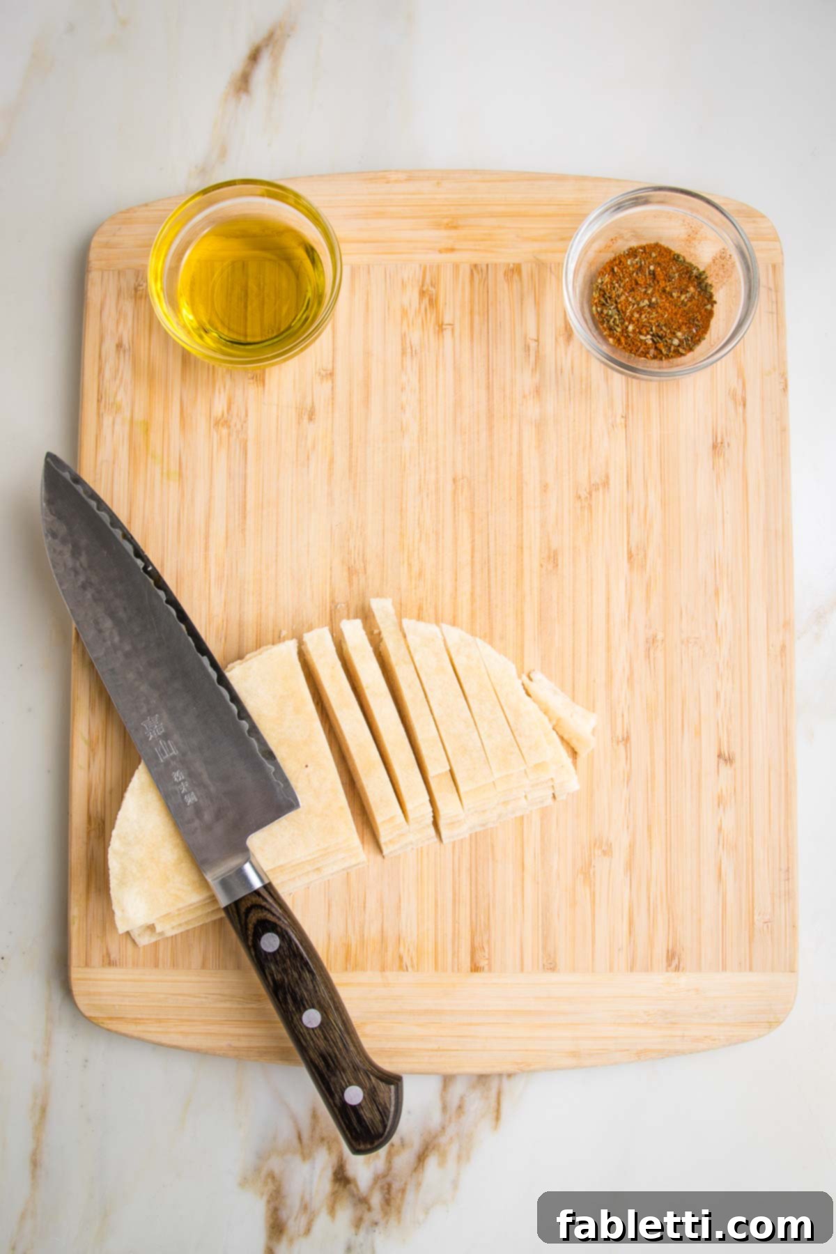 Hearty Vegan Taco Soup with Crispy Tortilla Strips 7 Almond flour tortillas stacked and being cut into strips on a wooden board. Also visible is a small dish of olive oil and another filled with taco seasonings.
