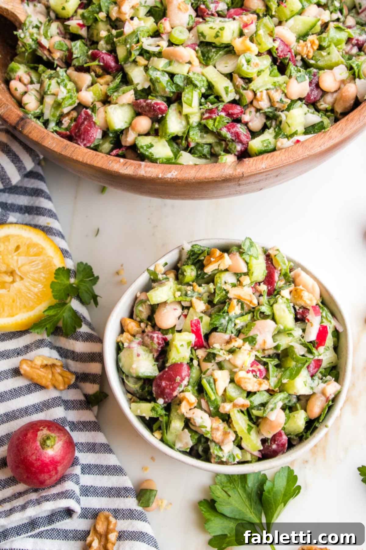 Zesty Kidney Bean Salad 2 Bean salad with greens and radishes.Large wooden bowl plus small white bowl with same salad. Whole lemon, walnuts, radish and fresh parsley leaves on the counter on a blue striped towel.