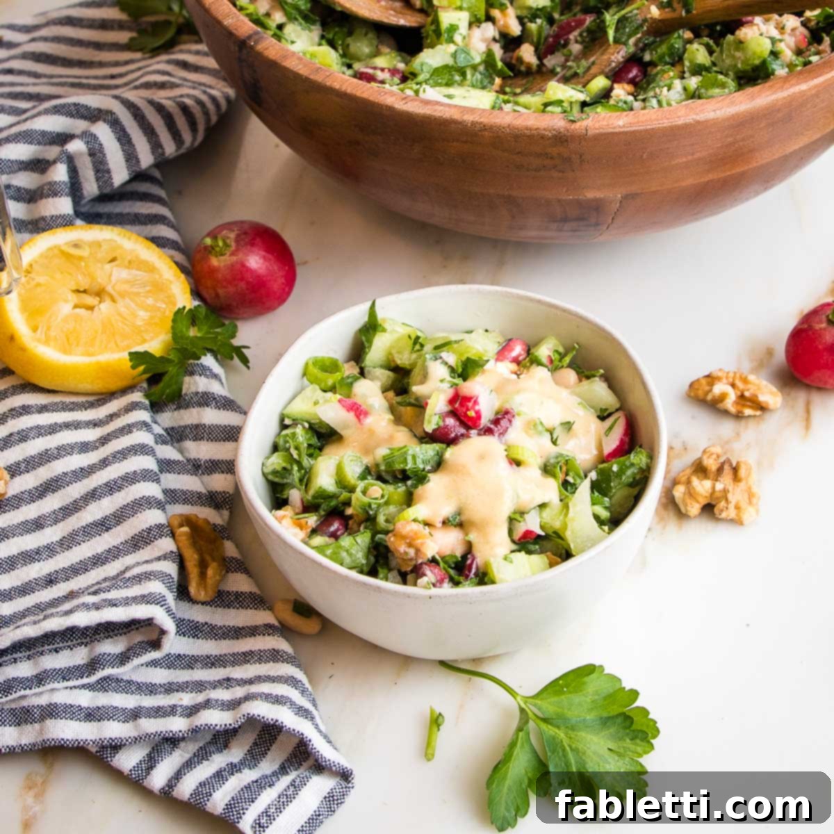 Zesty Kidney Bean Salad 11 white bowl filled with bean salad with lemon tahini dressing. larger bowl in the background along with lemon half, whole radishes and sprigs of fresh parsley.