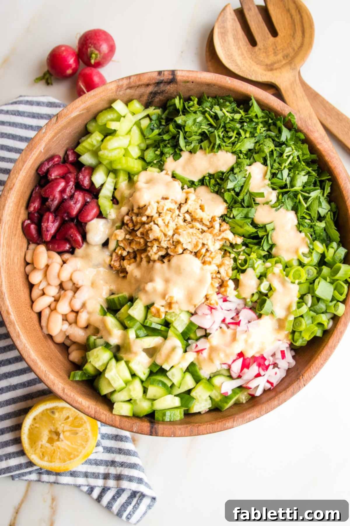 Zesty Kidney Bean Salad 4 Wooden bowl with sections of chopped veggies and a creamy dressing in the center: there's kidney beans, white beans, celery, cucumbers, radishes, scallions, chopped parsley and walnuts.