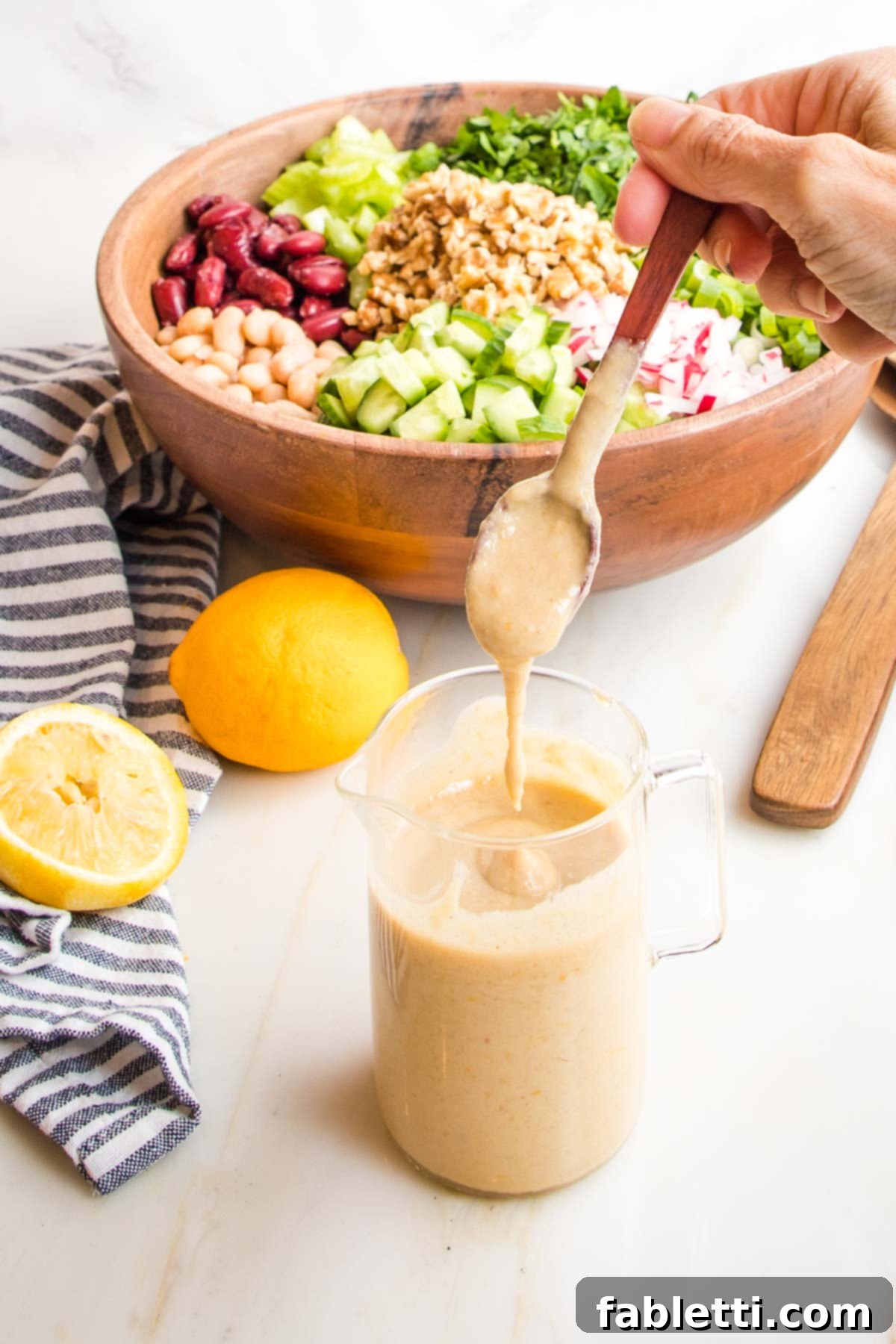 Zesty Kidney Bean Salad 8 small glass pitcher with creamy lemony dressing. there are lemons in the distance along with a wooden bowl filled with chopped veggies.