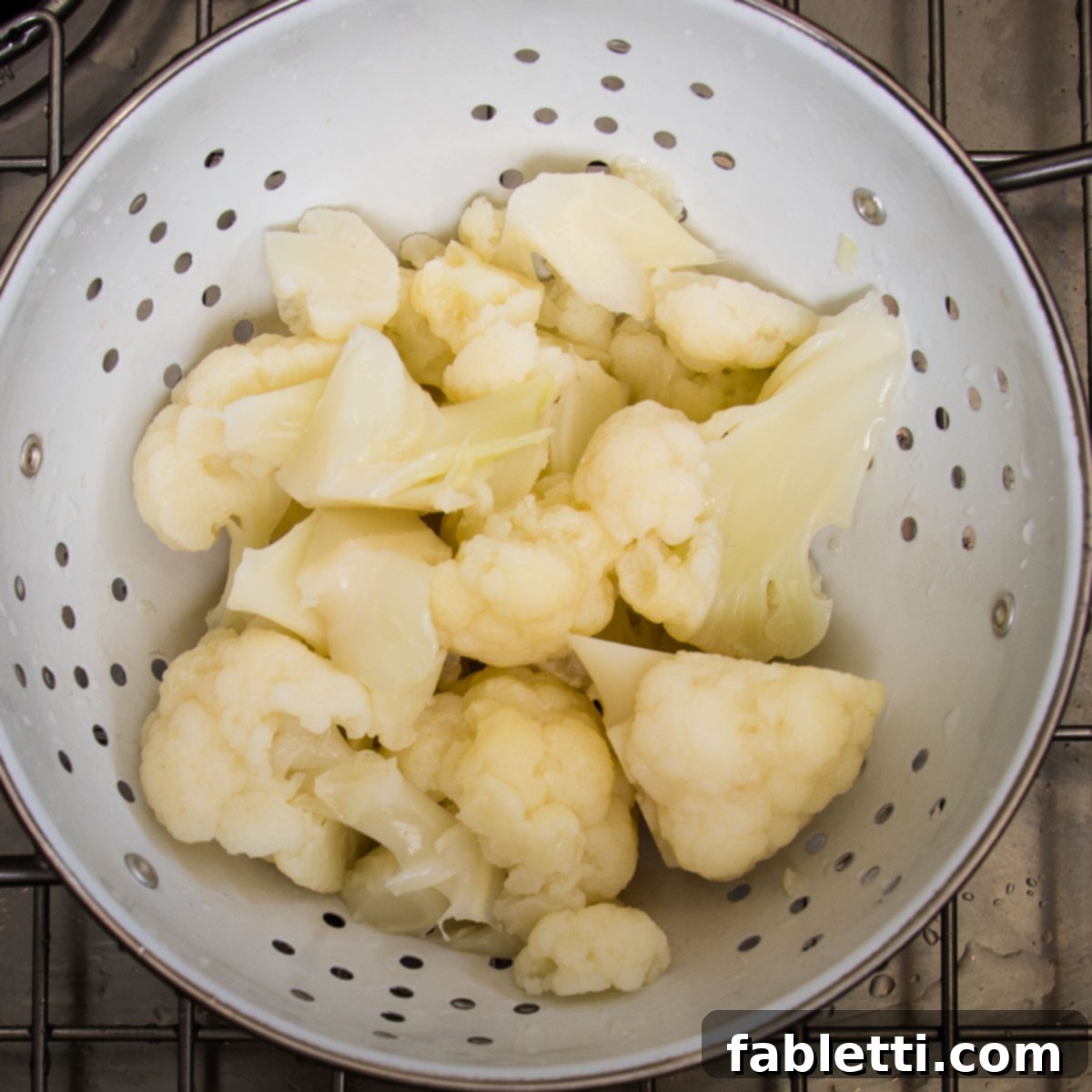 Steamed cauliflower draining in a white colander