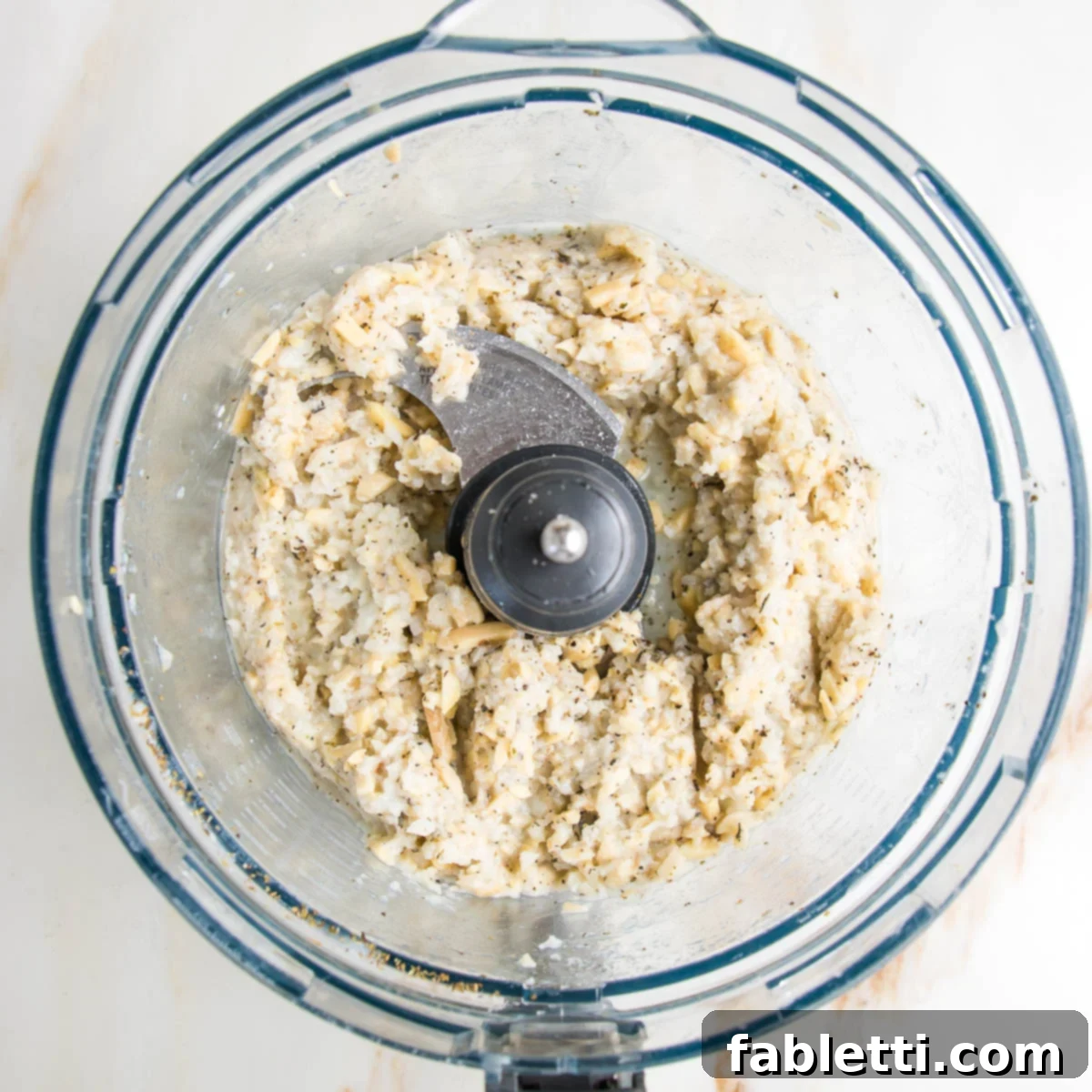 food processor bowl with chunks of partially blended cauliflower almond vegan ricotta.