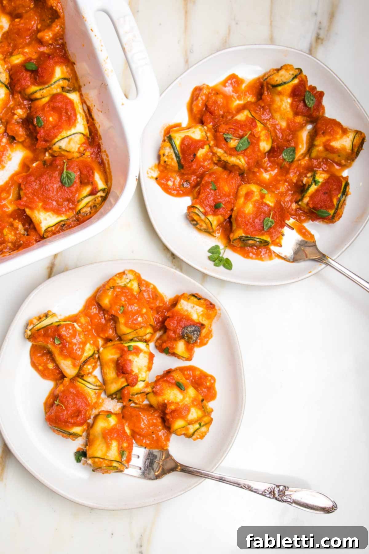 Plant-Based Zucchini Ricotta Rolls 2 White plate with zucchini roll ups filled with vegan ricotta and topped with marinara. Another plate full and the corner of the baking dish can be seen in the background.