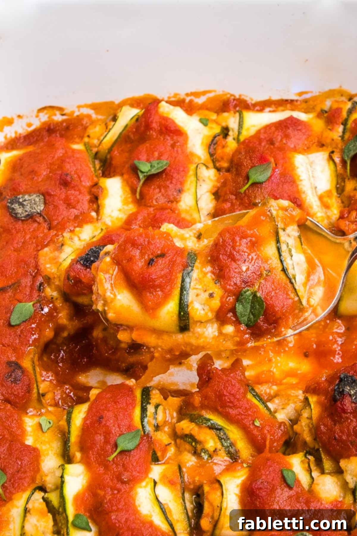 Plant-Based Zucchini Ricotta Rolls 3 Close-up of a fork holding a zucchini roll filled with ricotta and marinara, with more roll ups in the background.