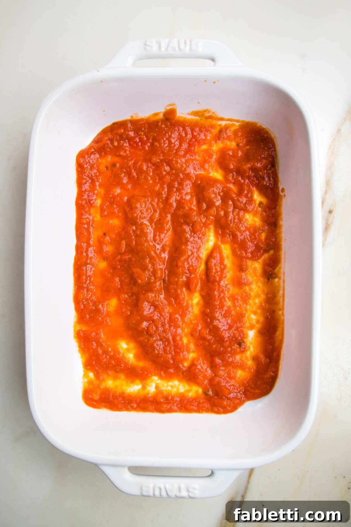 Plant-Based Zucchini Ricotta Rolls 7 White baking pan with a thin layer of bright red marinara sauce spread on the bottom.