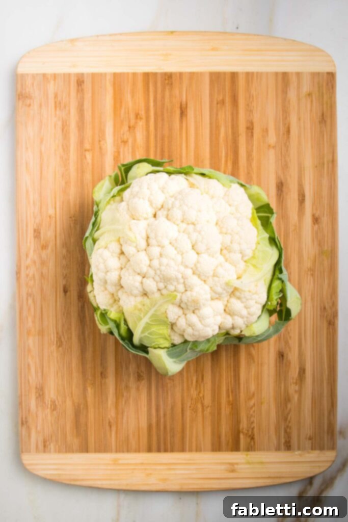 Whole head of cauliflower resting on a bamboo wooden cutting board.