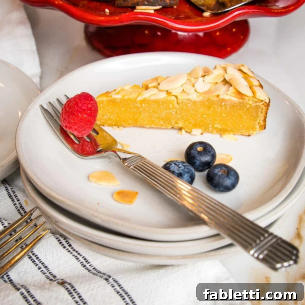 Side view of a piece of lemon cake on a white rimmed plate with a few blueberries and a raspberry plus a few sliced almonds on the plate. 