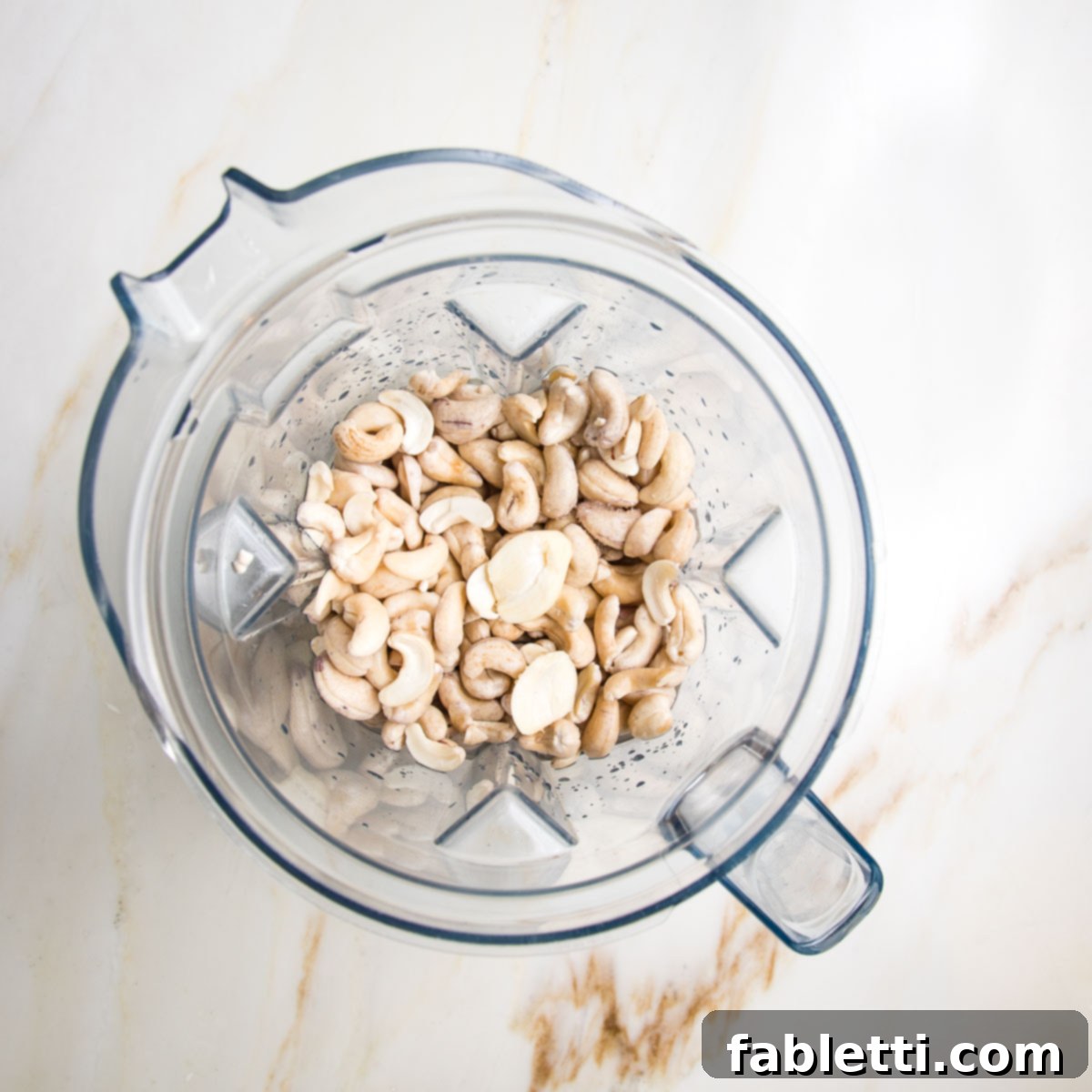 Blender pitcher filled with soaked cashews, salt, lemon juice, vinegar, garlic and water.