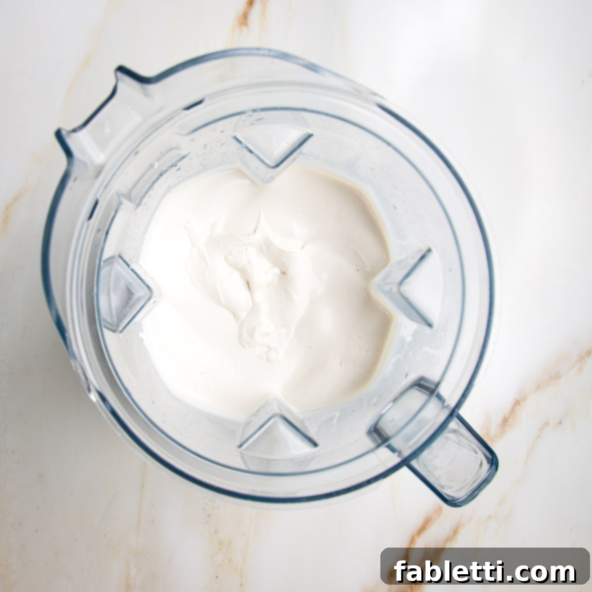 Blender pitcher filled with creamy white vegan sour cream.