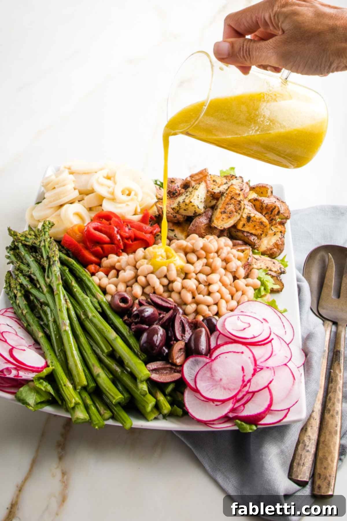 Vibrant Vegan Nicoise 12 Lemon Vinaigrette being poured over a vegan nicoise salad in colorful sections on a large white platter.