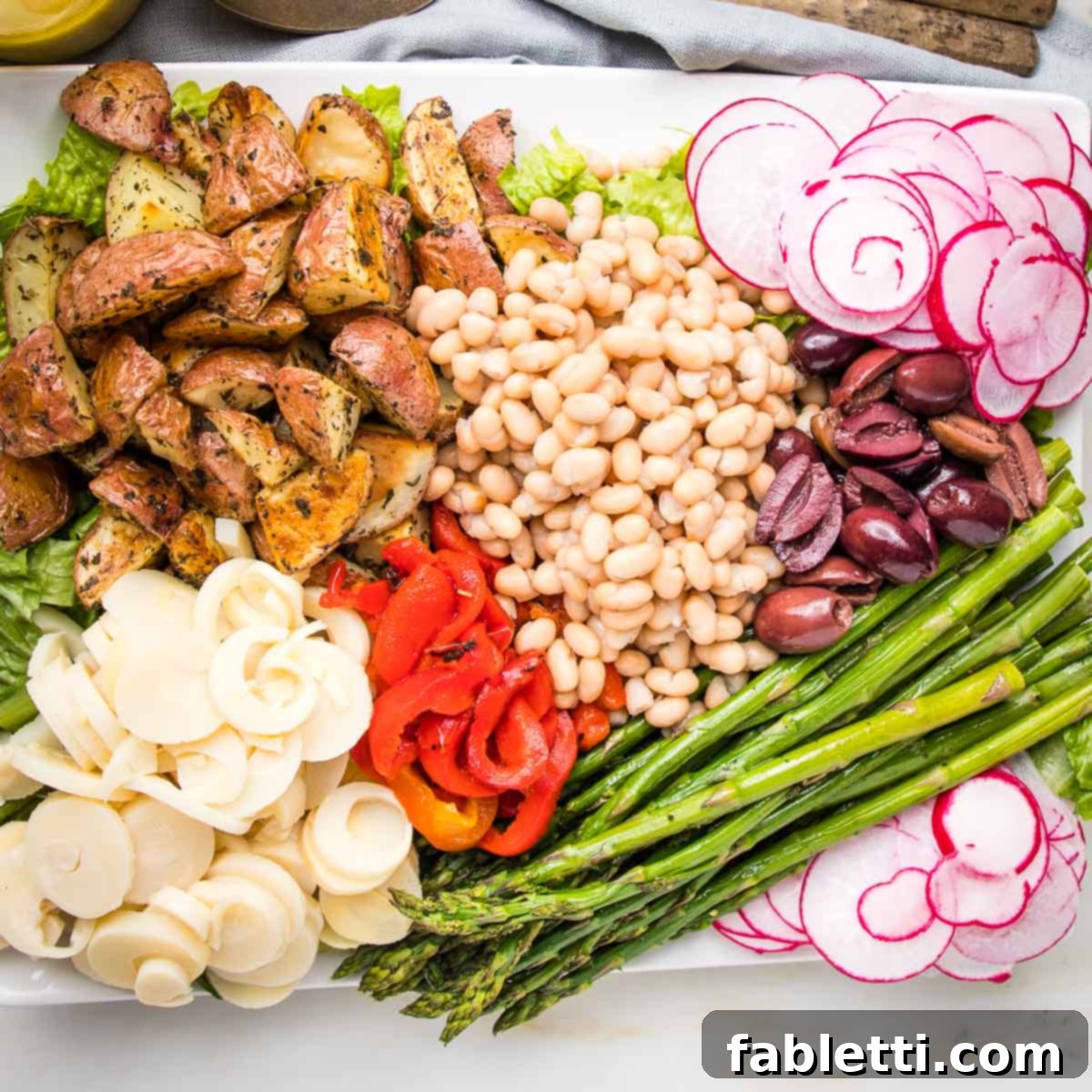 Vibrant Vegan Nicoise 13 Composed nicoise salad with potatoes, hearts of palm, red peppers, asparagus, radish, small white beans and olives.