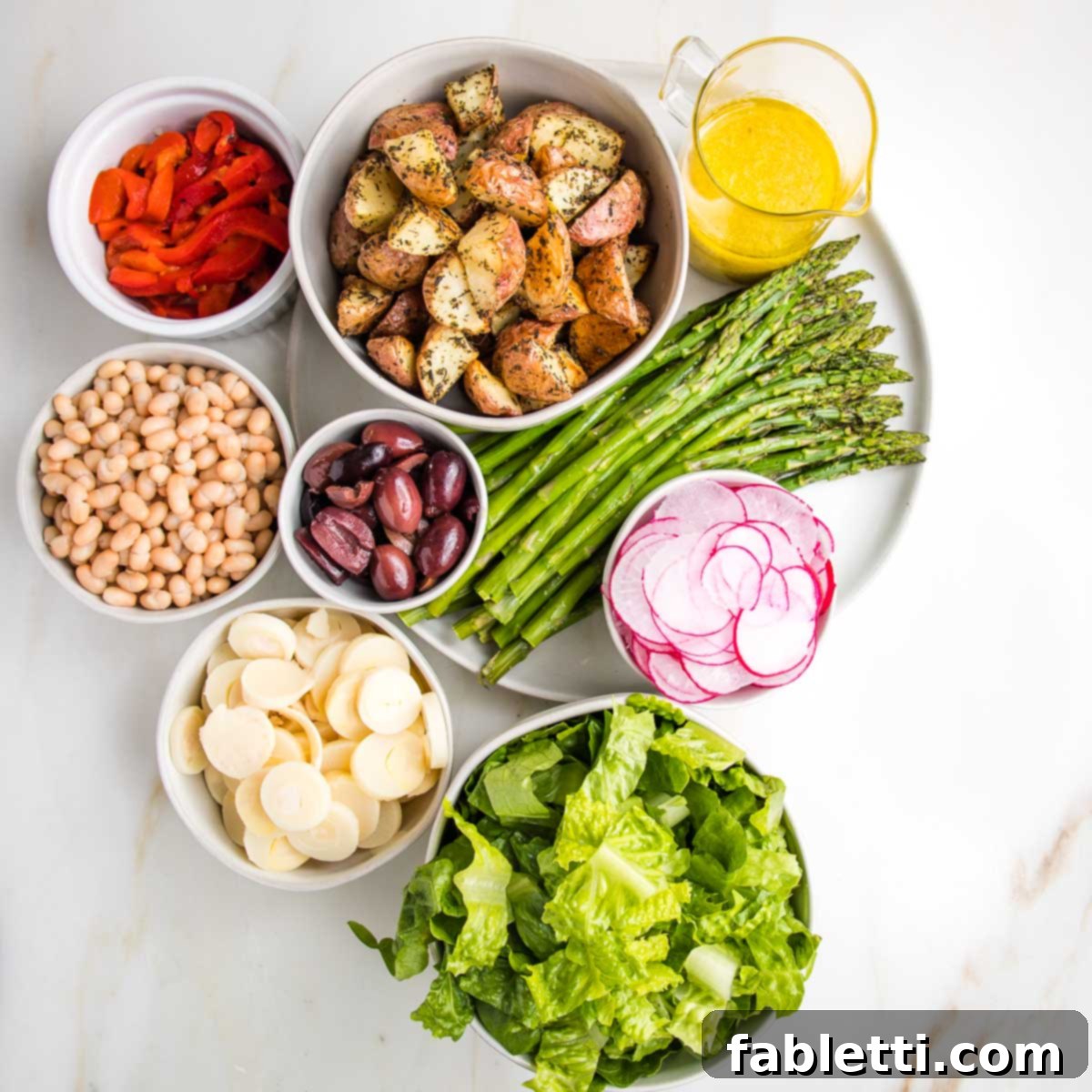 Vibrant Vegan Nicoise 4 White dishes with separate ingredients for nicoise salad: roasted red pepper strips, roasted potatoes, lemon vinaigrette, roasted asparagus, small white beans, kalamata olives, slice hearts of palm, sliced radish and romaine lettuce.