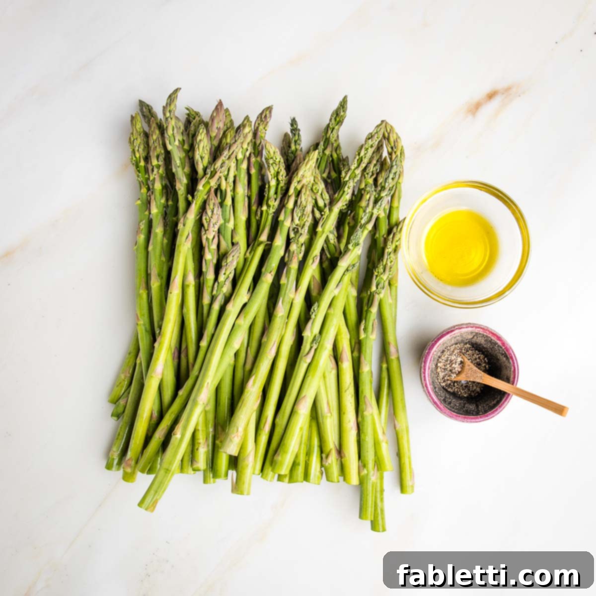 Vibrant Vegan Nicoise 7 Fresh asparagus and a small glass dish of olive oil and a little container with fresh black pepper and a small wooden spoon.